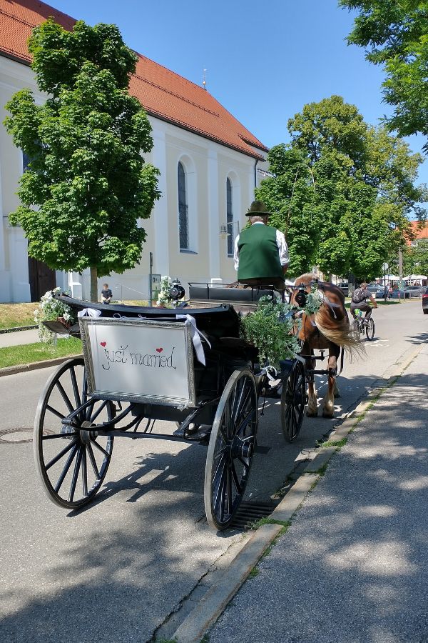 Vor einer Kirche wartet eine Pferdekutsche auf ein Hochzeitspaar.
