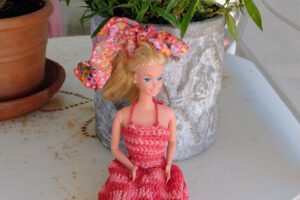 Barbie sitzt vor einem Blumentopf.