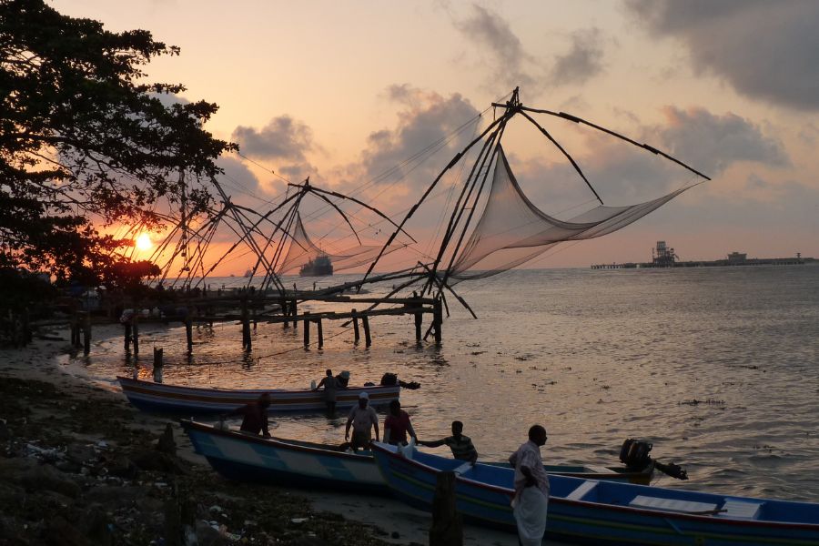 Fischernetze und Boote bei Sonnenuntergang im indischen Kochi, Kerala.