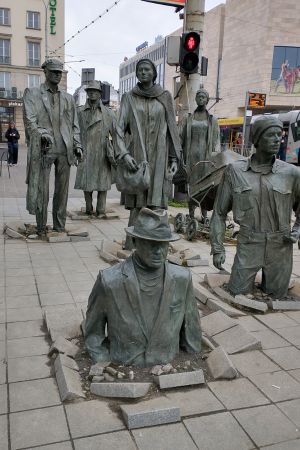 Eine Gruppe von sieben Skulpturen versinkt langsam im Bürgersteig.