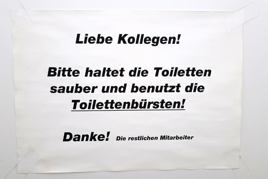 Anschlag an der Toilettentür: "Liebe Kollegen! Bittet haltet die Toiletten sauber und benutzt die Toilettenbürsten! Danke! Die restlichen Mitarbeiter"