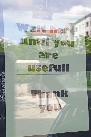 An einer Fensterscheibe hängt ein Zettel mit der Aufschrift "Wait here until you are useful. Thank you".