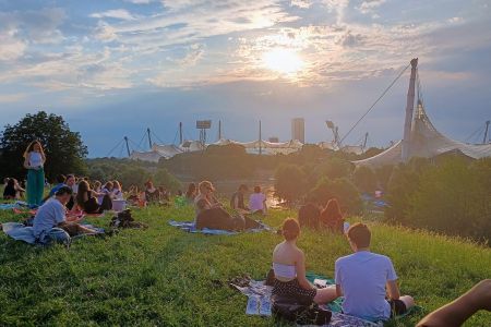 Menschen auf dem Münchener Olympiaberg, mit Blick auf das Olympiastadion und die untergehende Sonne.